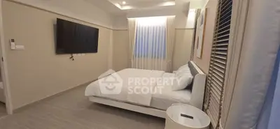 Modern bedroom with sleek design, featuring a wall-mounted TV and elegant window drapes.