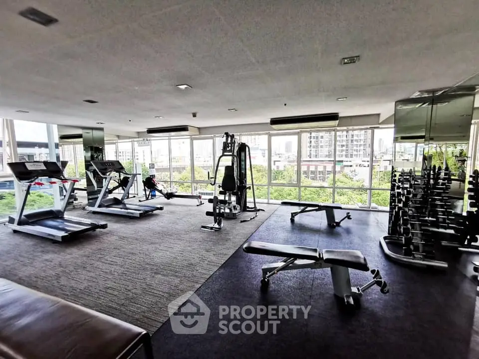 Spacious gym with modern equipment and city view, perfect for fitness enthusiasts.