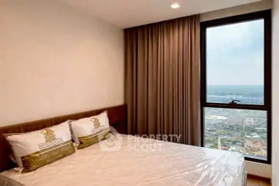 Modern bedroom with large window offering stunning city view, featuring elegant curtains and cozy bedding.