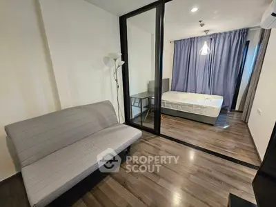Modern apartment with glass partition separating living area and bedroom, featuring sleek flooring.