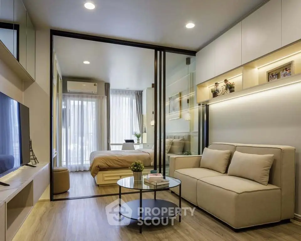 Modern open-layout living room with glass partition to bedroom, featuring sleek furniture and ambient lighting.