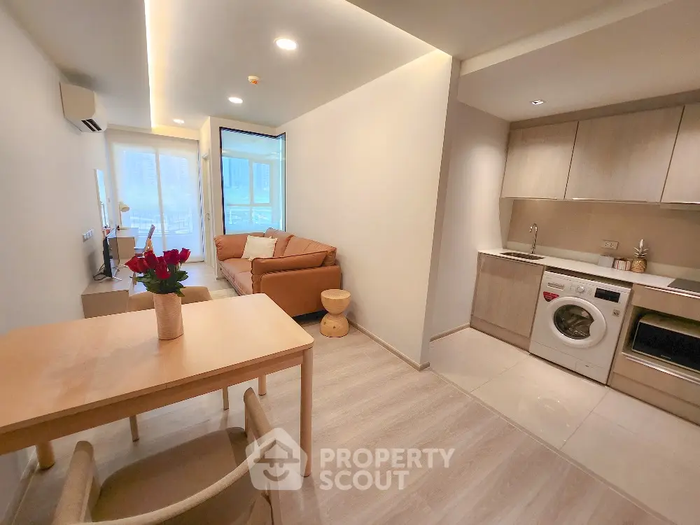 Modern open-plan living room with kitchen featuring washing machine and cozy seating area.