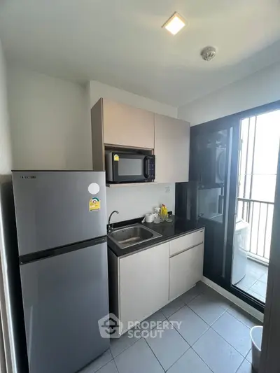 Modern compact kitchen with fridge, microwave, and balcony access
