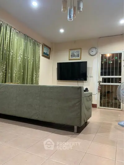 Cozy living room with green sofa, wall-mounted TV, and elegant curtains.