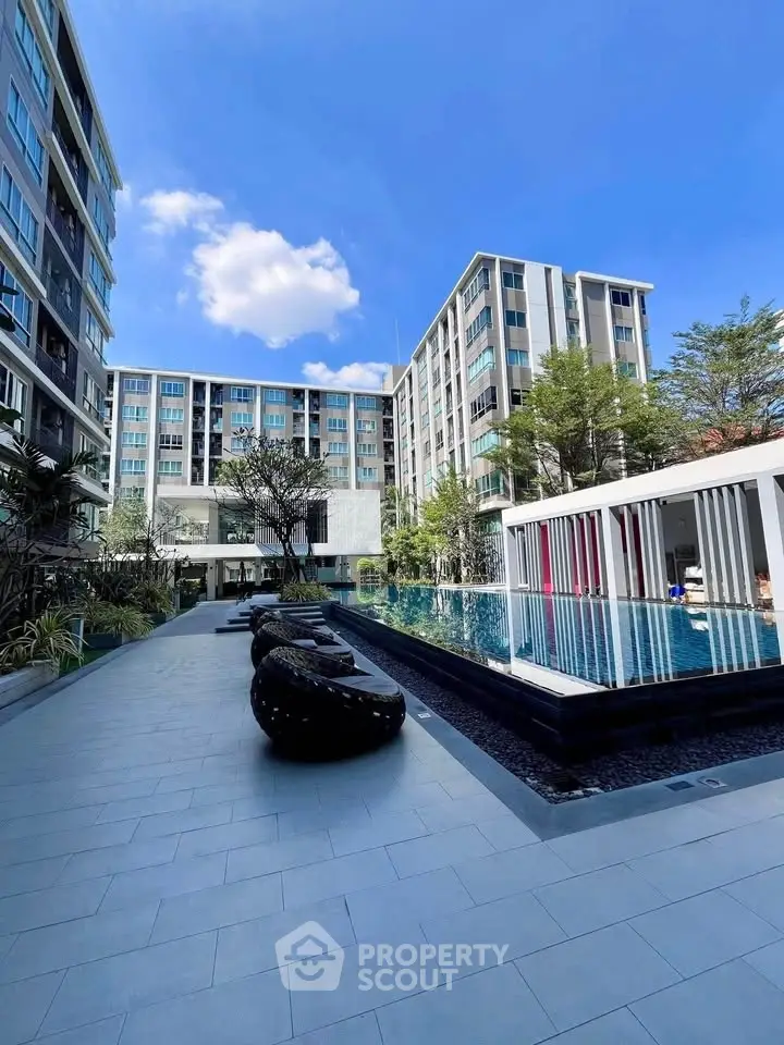 Modern apartment complex with pool and outdoor seating under blue sky.
