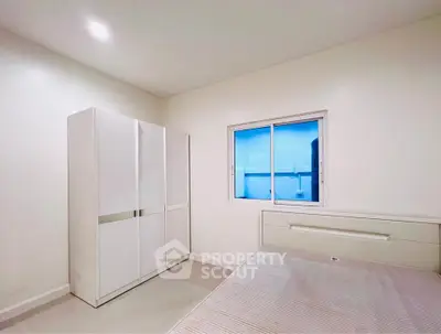 Modern minimalist bedroom with sleek white furniture and large window.
