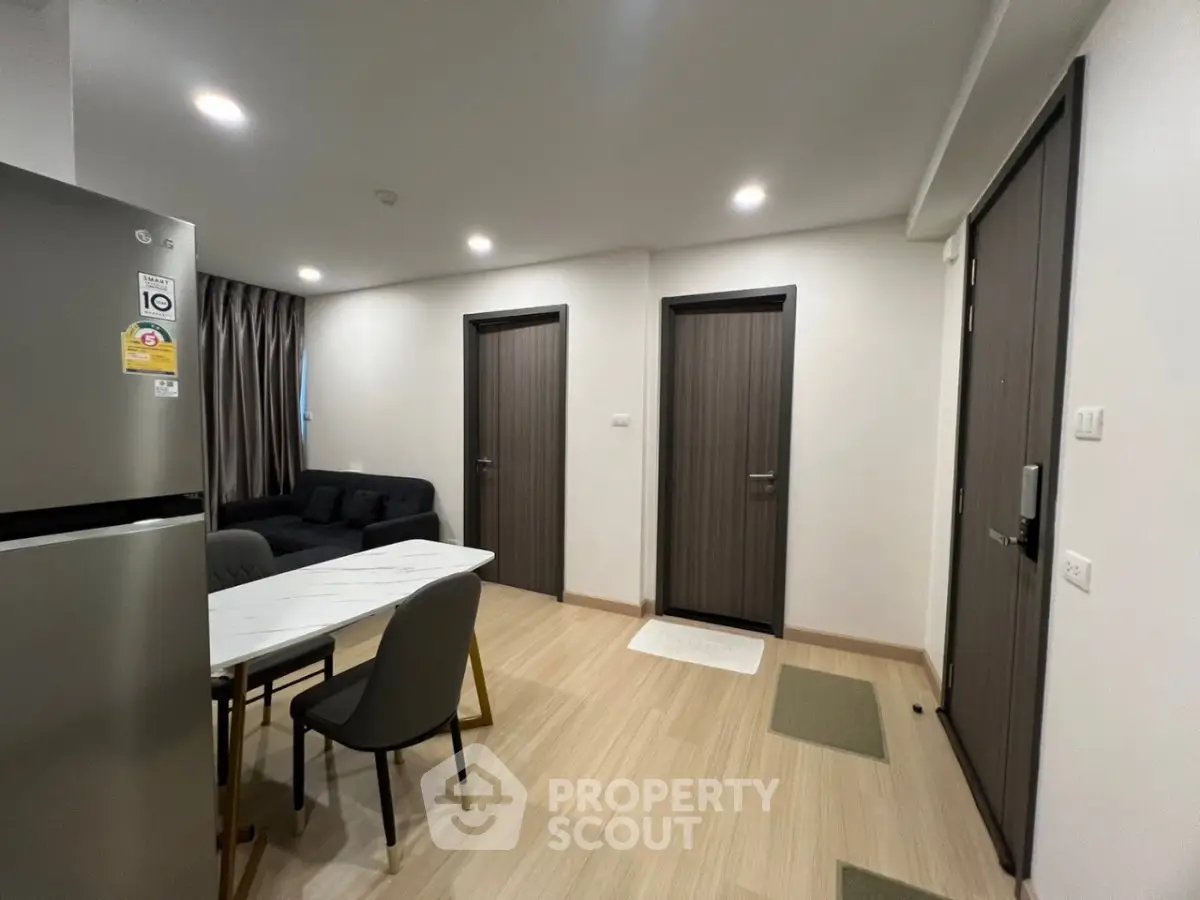 Modern apartment interior with dining area and living room, featuring sleek furniture and wooden flooring.