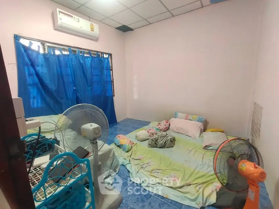 Cozy bedroom with air conditioning and fans, featuring a simple bed setup and blue curtains.