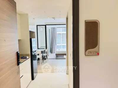 Modern apartment interior with open kitchen and view into bedroom, featuring sleek design and natural light.