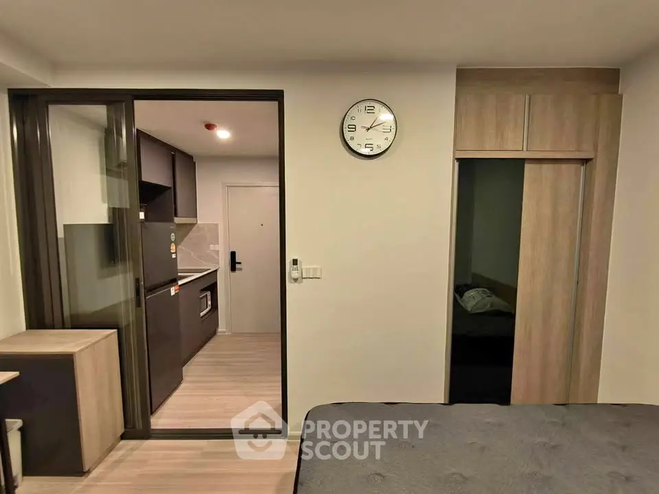 Modern studio apartment with sleek kitchen and cozy bedroom area, featuring a sliding glass door and wall clock.