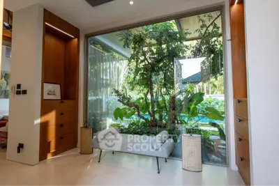 Luxurious living room with large window view of lush garden, featuring modern furniture and elegant wooden accents.