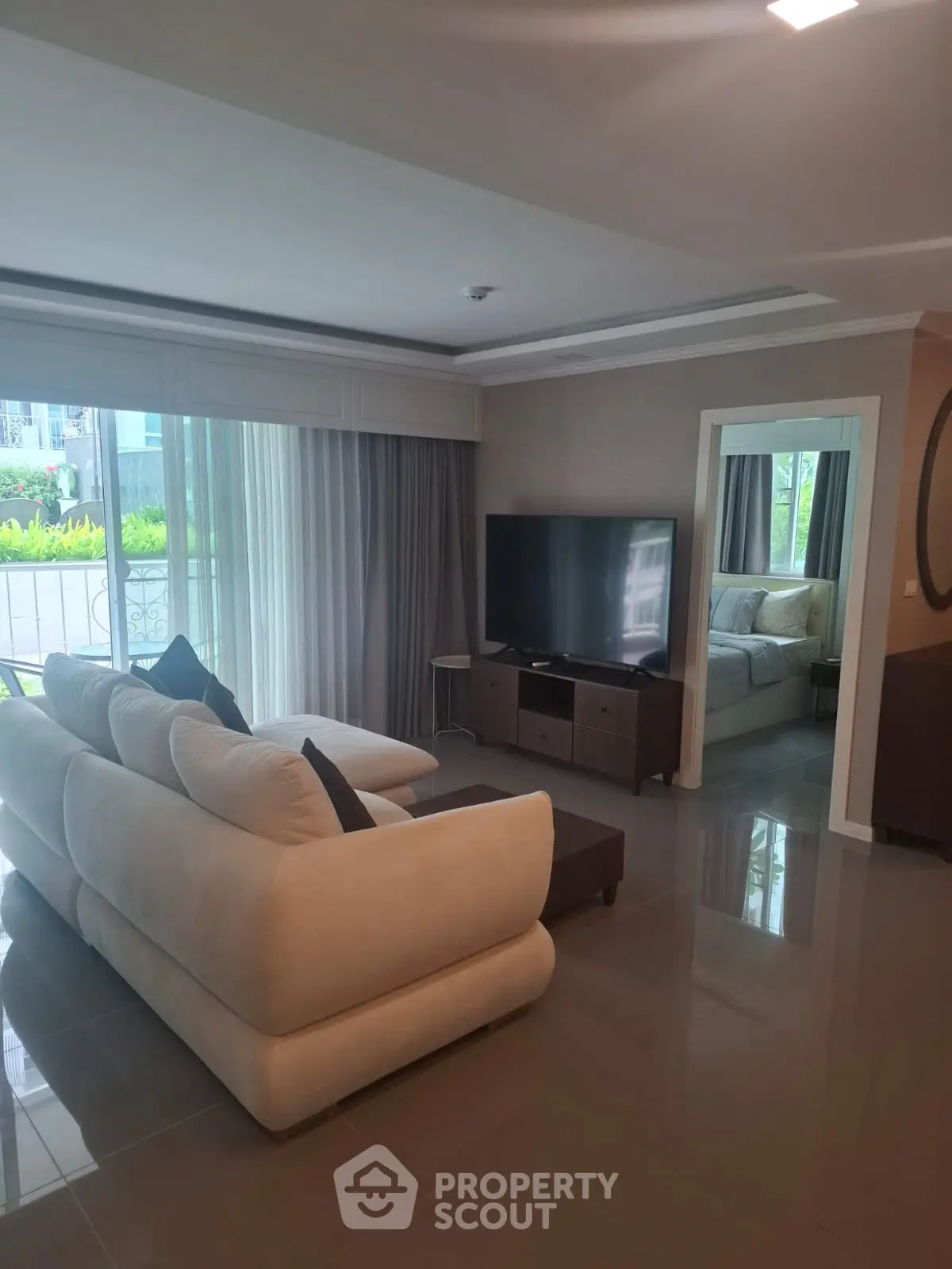 Spacious living room with modern decor and large TV, featuring a cozy sofa and natural light from large windows.