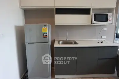 Modern kitchen with sleek cabinetry, stainless steel fridge, and microwave in a stylish apartment.