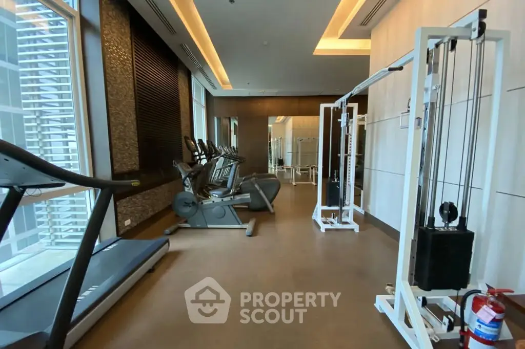 Modern gym with state-of-the-art equipment and large windows in luxury building.