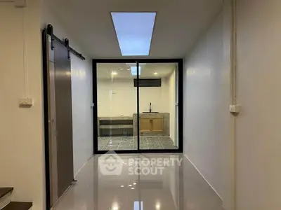 Modern interior with sleek sliding door and glass partition, featuring a stylish kitchen area.