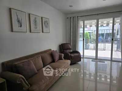 Charming living room with cozy sofa and recliner, large glass doors opening to a bright outdoor view.