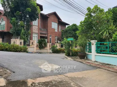 Charming red brick house with lush greenery and gated entrance in a serene neighborhood.