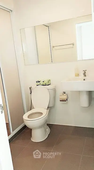 Modern bathroom with sleek fixtures and neutral tiles, featuring a large mirror and compact design.