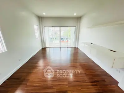 Spacious living room with wooden flooring and large windows offering natural light.
