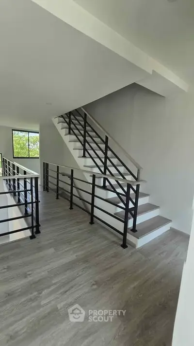 Modern staircase with sleek railing in a bright, open interior space with large window view.