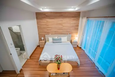 Spacious bedroom with modern decor and wooden flooring, featuring a cozy bed and natural light.
