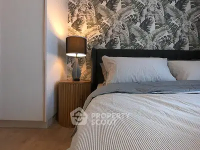 Stylish bedroom with modern decor and tropical wallpaper, featuring a cozy bed and elegant bedside lamp.