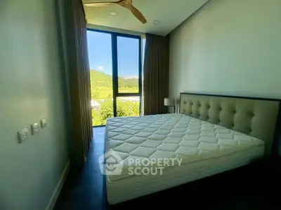 Modern bedroom with large window offering scenic view, featuring a stylish bed and ceiling fan.