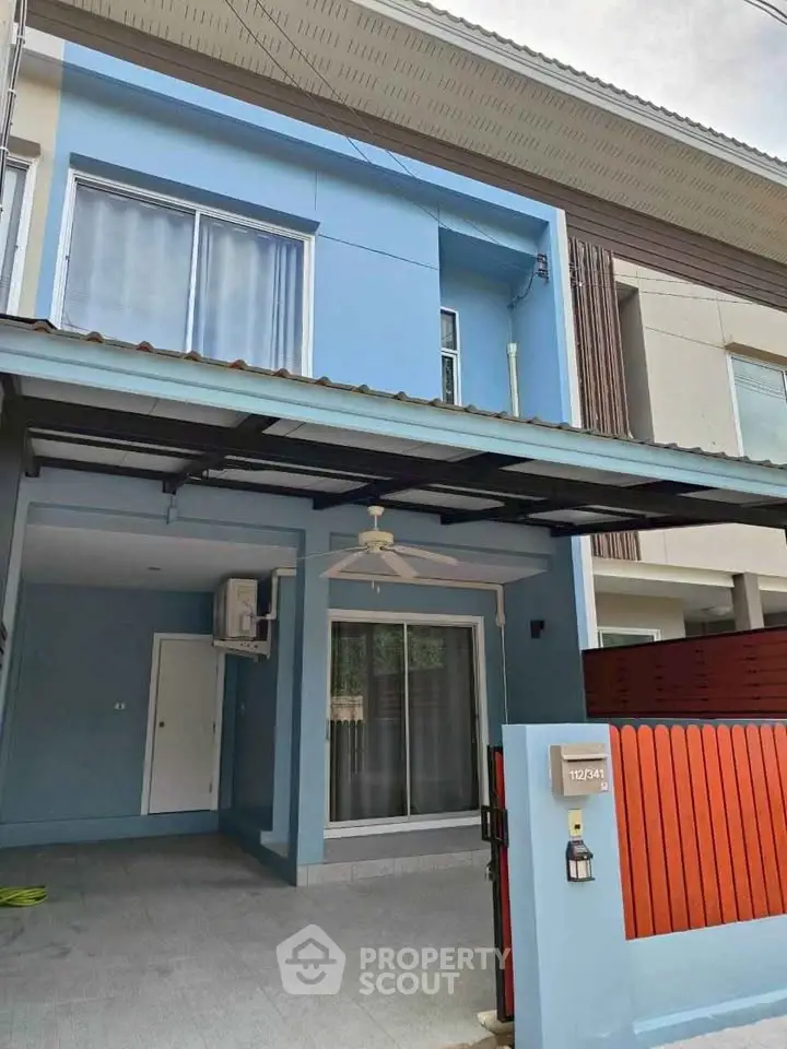 Modern two-story blue townhouse with covered parking and red fence