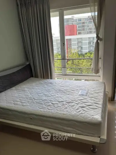 Bright bedroom with large window offering city view, featuring a comfortable bed and elegant curtains.