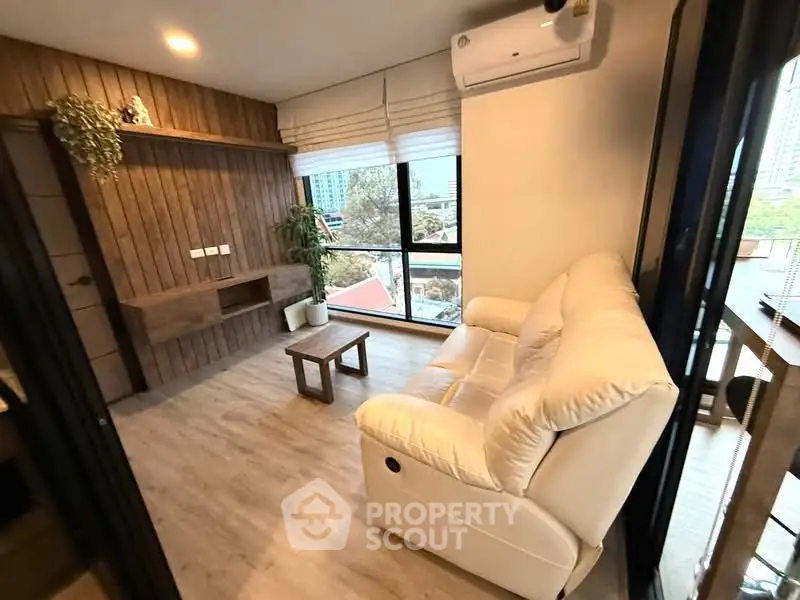 Modern living room with cozy sofa and wooden accents, featuring large windows with city view.