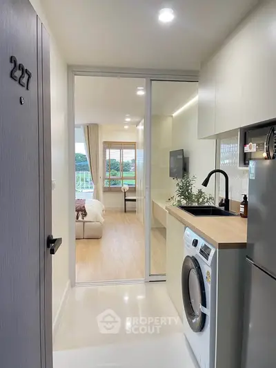 Modern apartment interior with open kitchen and cozy living area, featuring a washing machine and scenic view.