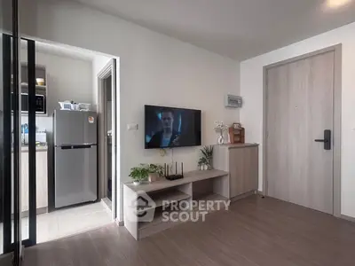 Modern living room with sleek wooden flooring, wall-mounted TV, and adjacent kitchen area with stainless steel fridge.