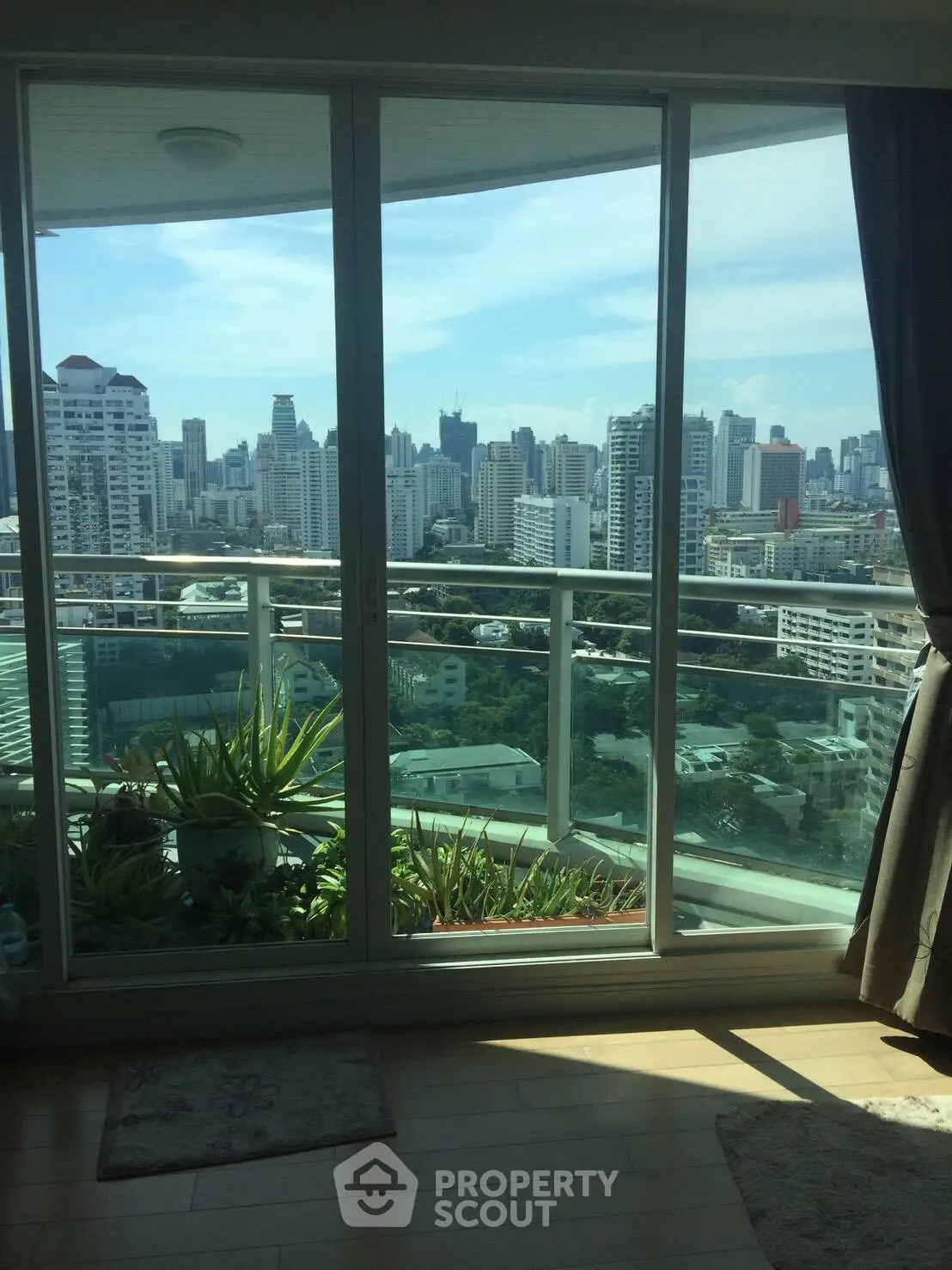 Stunning city view from a high-rise apartment balcony with lush greenery.