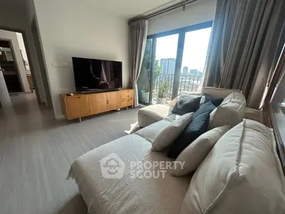Modern living room with large TV, cozy sofa, and city view from balcony.
