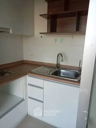 Compact kitchen with modern cabinetry and stainless steel sink in cozy apartment.