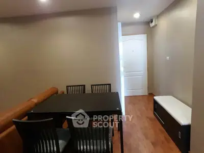 Modern dining area with sleek black table and chairs, adjacent to cozy living space with wooden flooring.