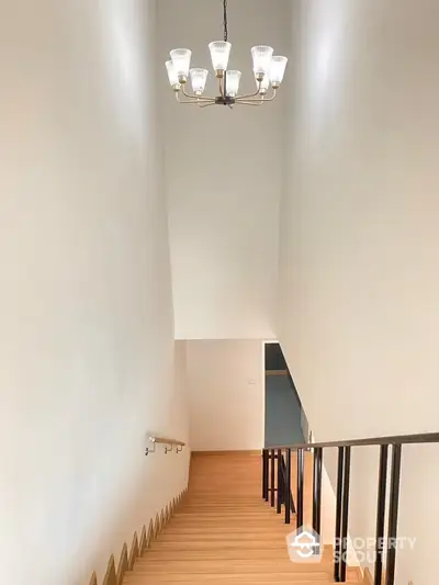 Elegant staircase with modern chandelier, wooden steps, and sleek metal balusters, leading to a bright, inviting upper level.