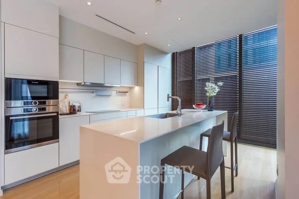 Modern kitchen with sleek design, featuring an island, built-in oven, and stylish blinds.