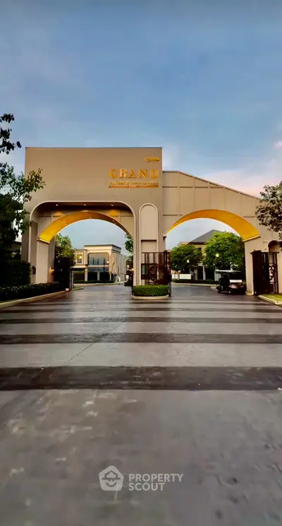 Elegant entrance of a luxury residential complex with grand archway and lush greenery.