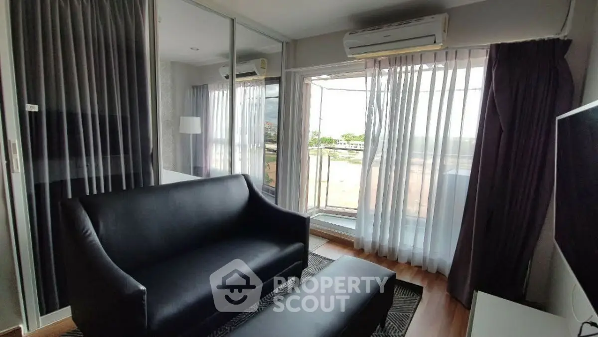 Modern living room with sleek black sofa and large windows offering natural light and scenic views.