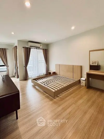 Spacious modern bedroom with wooden flooring and large windows for natural light.