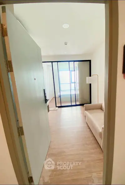 Modern apartment entrance with cozy living area and glass partition, featuring sleek flooring and natural light.