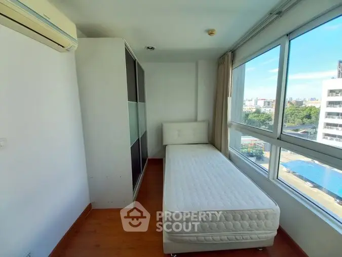 Bright and airy bedroom with large windows offering a view, complemented by a single bed and built-in wardrobe, perfect for urban living.