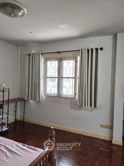 Cozy bedroom with wooden flooring and window with curtains, perfect for a peaceful retreat.