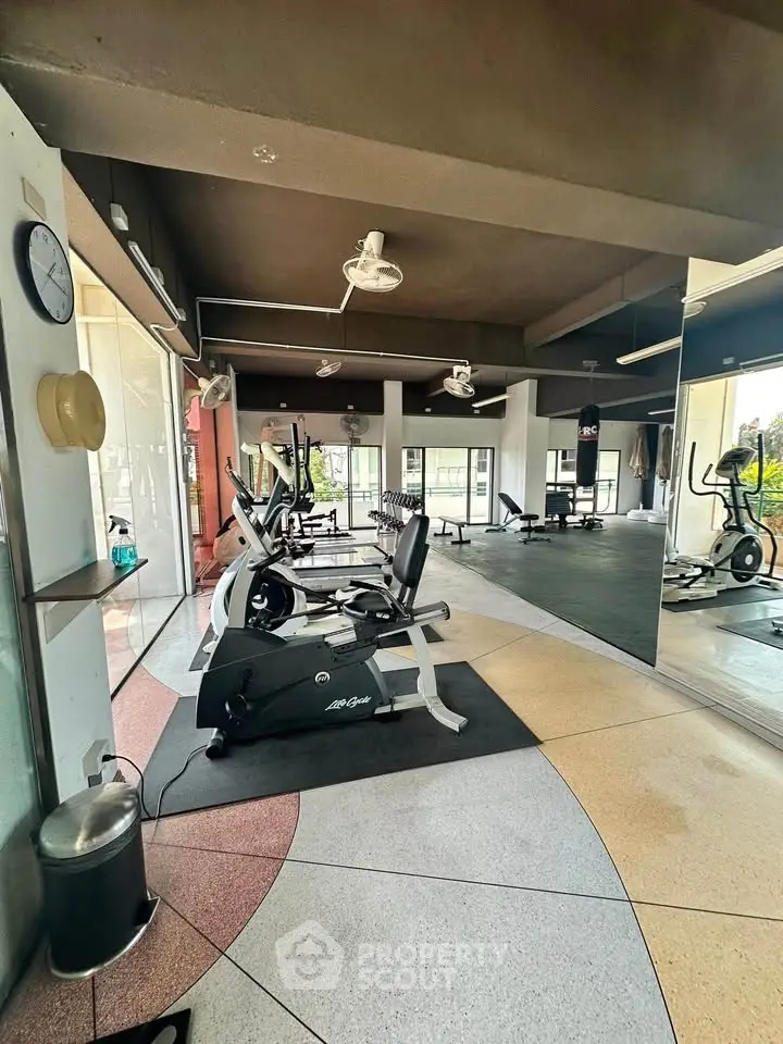 Spacious gym with modern exercise equipment and large mirrors in a well-lit area.