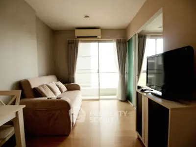 Modern living room with cozy sofa and large TV, featuring natural light from balcony windows.