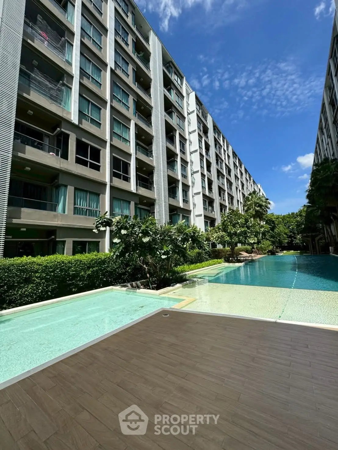 Luxurious condominium with stunning pool and lush greenery under a clear blue sky.