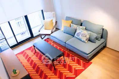 Stylish living room with modern sofa, vibrant rug, and large windows offering natural light.