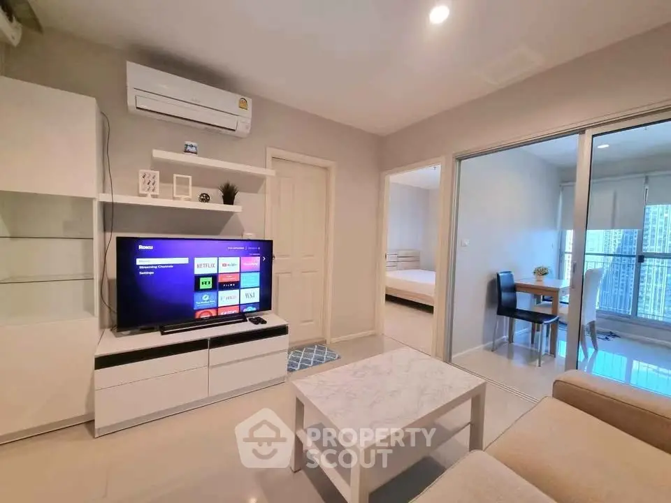 Modern living room with sleek furniture and smart TV, open layout to dining area with city view.