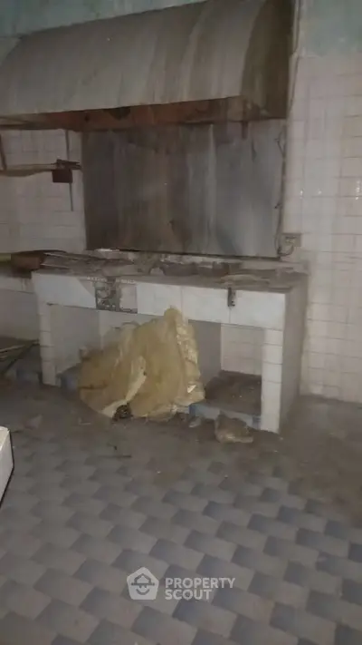 Old kitchen with damaged stove and tiled walls, needs renovation.